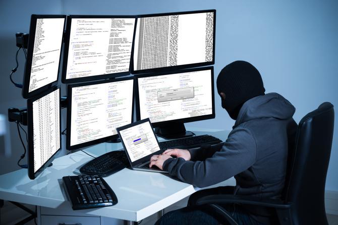 Een hacker werkt op een laptop en veel schermen om gegevens te stelen